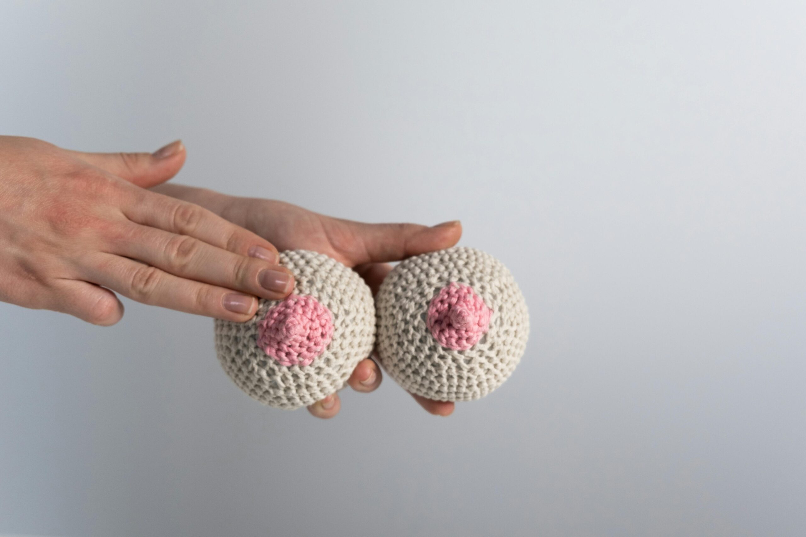 Hand touching knitted yarn breasts for breast cancer awareness campaign.